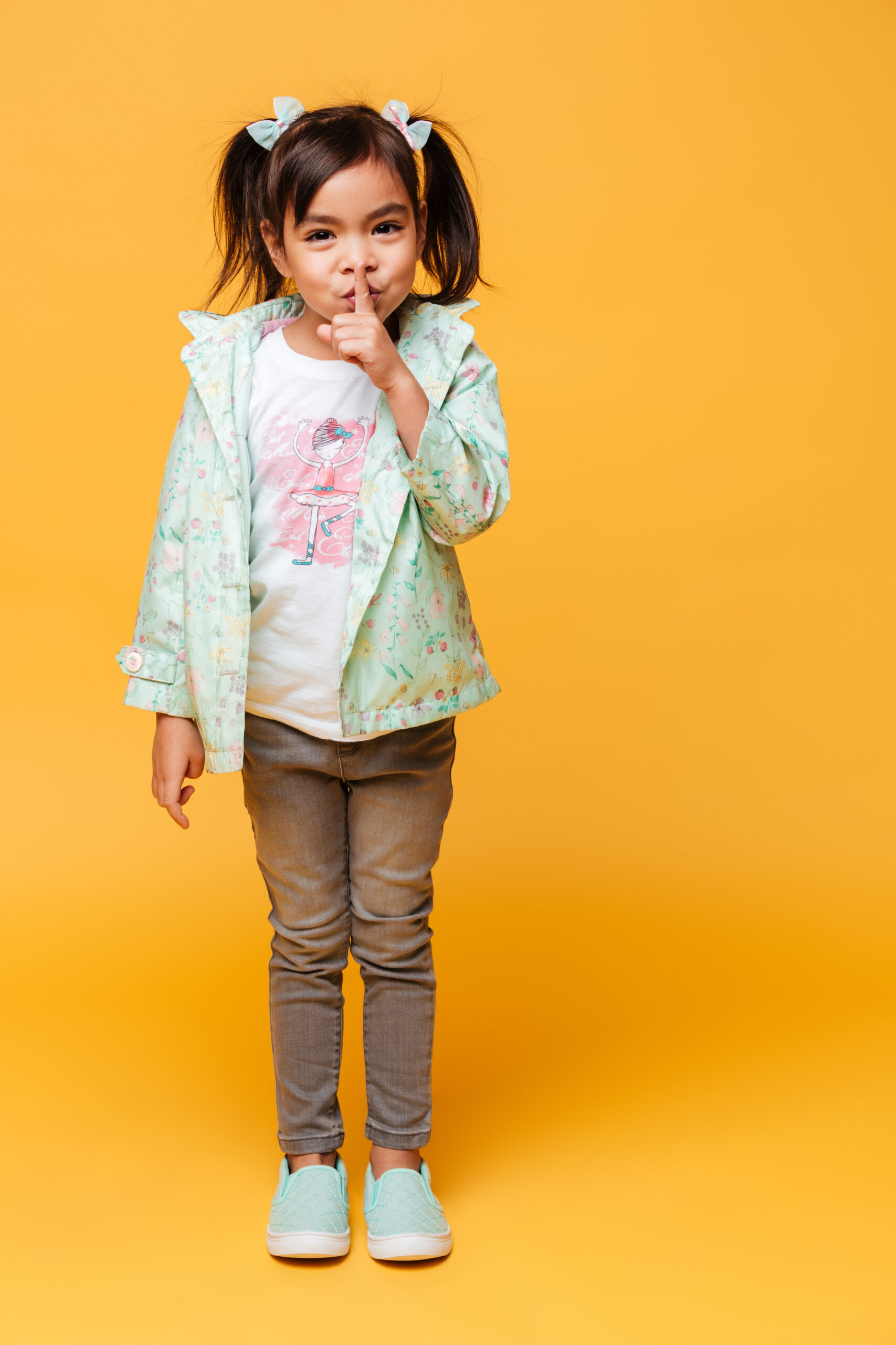 Picture of cute little girl child standing isolated over yellow background. Looking camera showing silence gesture.